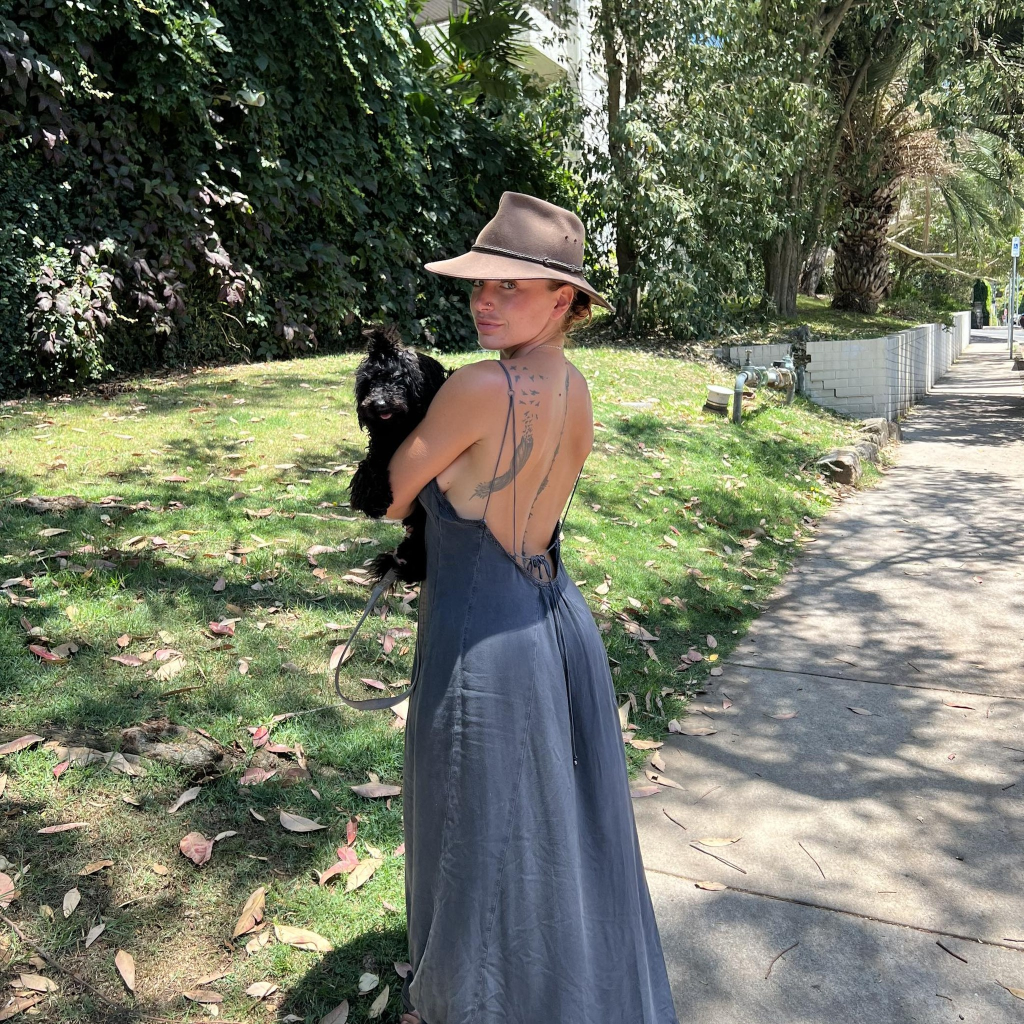 Delina Stevenson in a sunhat and backless dress holding a black dog.