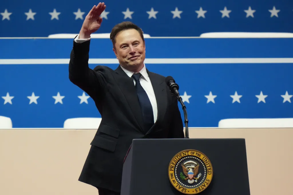Elon Musk speaking at a podium with the Seal of the President of the United States.