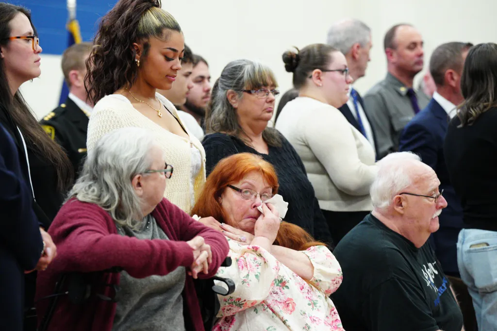 Attendees at a press conference, with a woman in the foreground wiping her eyes with a tissue.