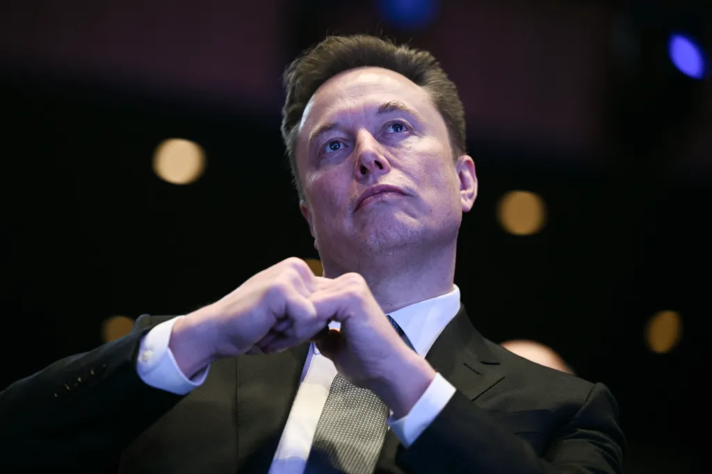 Elon Musk looking upward with his hands clasped.