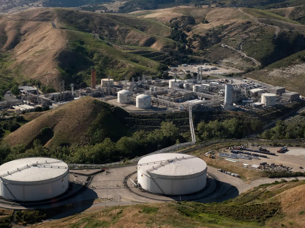 Aerial view of Sable Offshore’s Las Flores Canyon facility in Goleta, California, showing large storage tanks, industrial buildings, and pipes nestled in hills.