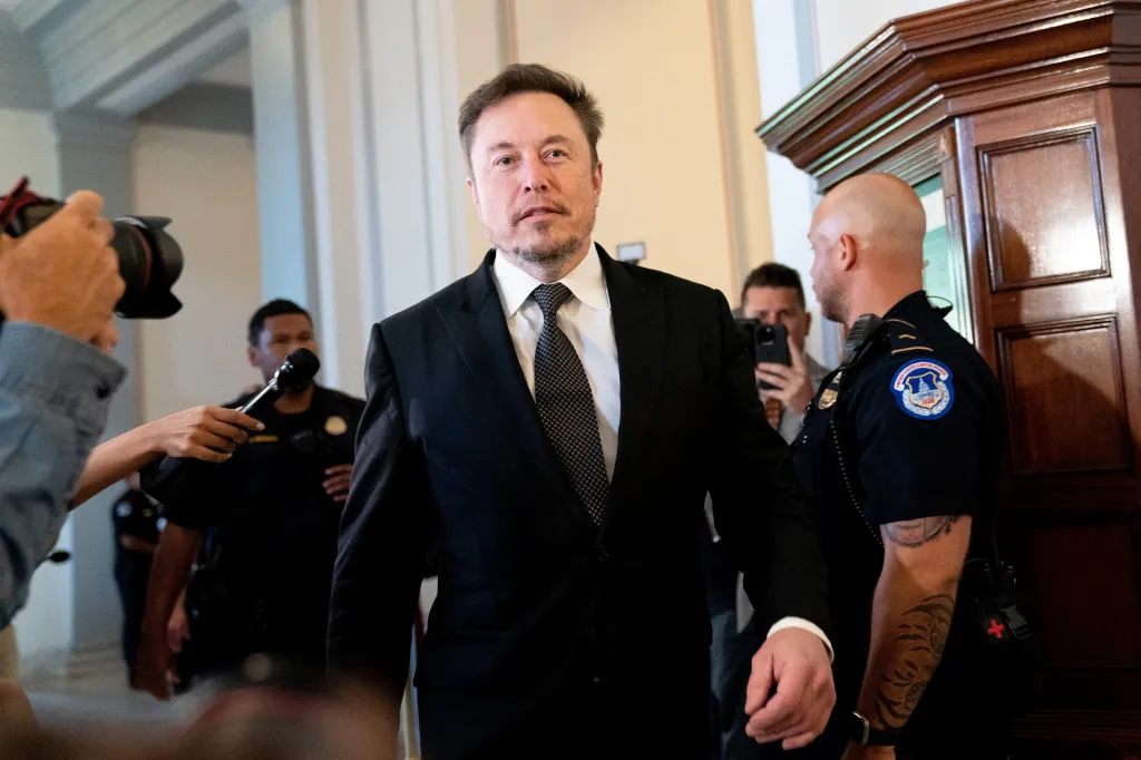 Elon Musk walks through a crowd of photographers and security guards.