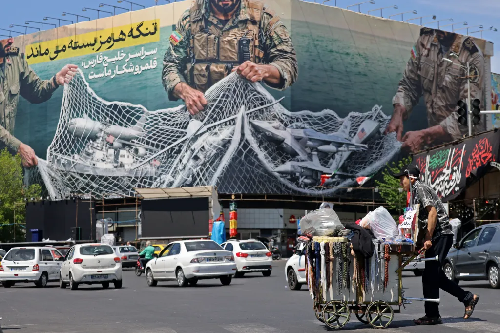A vendor pushes his cart past a billboard with soldiers pulling a net of US military equipment, reading 'The Strait of Hormuz remains closed' in Tehran.
