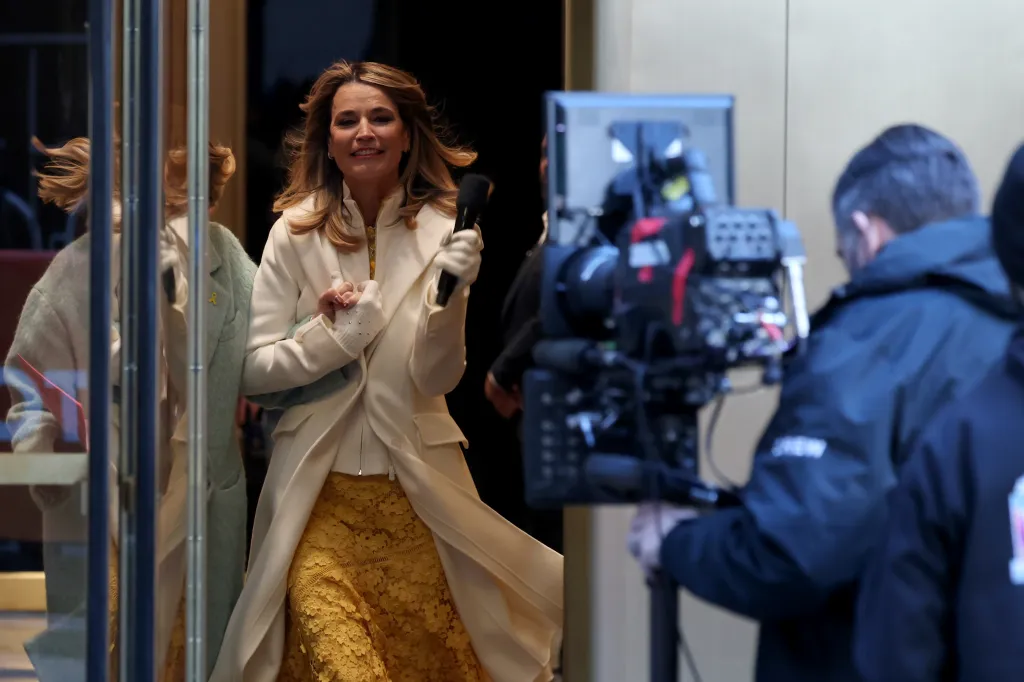 Savannah Guthrie holds a microphone while being embraced by a colleague as she returns to the "Today" show.