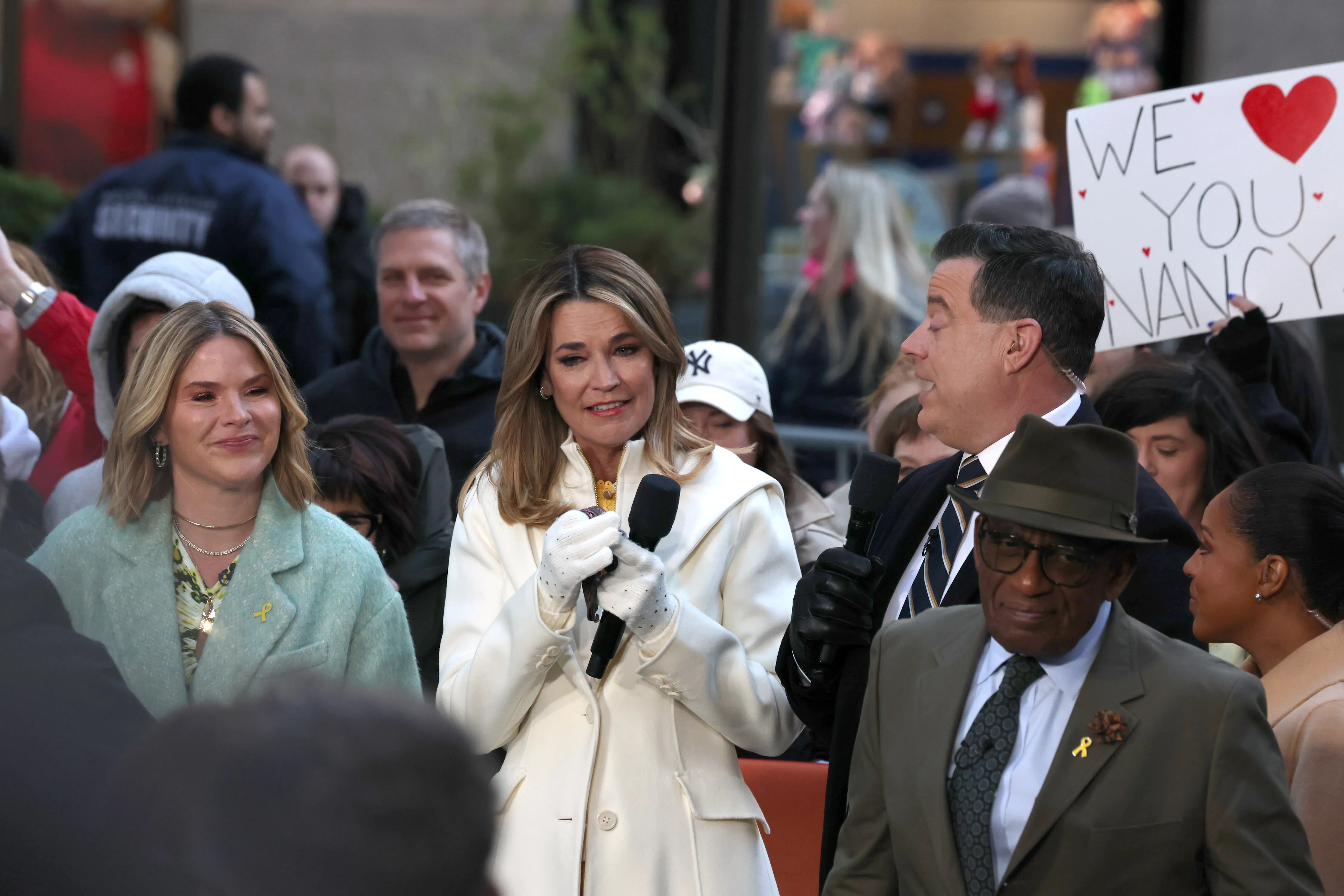 Savannah Guthrie, wearing a white coat and white gloves, holding a microphone, appearing emotional on her return to the "Today" show.