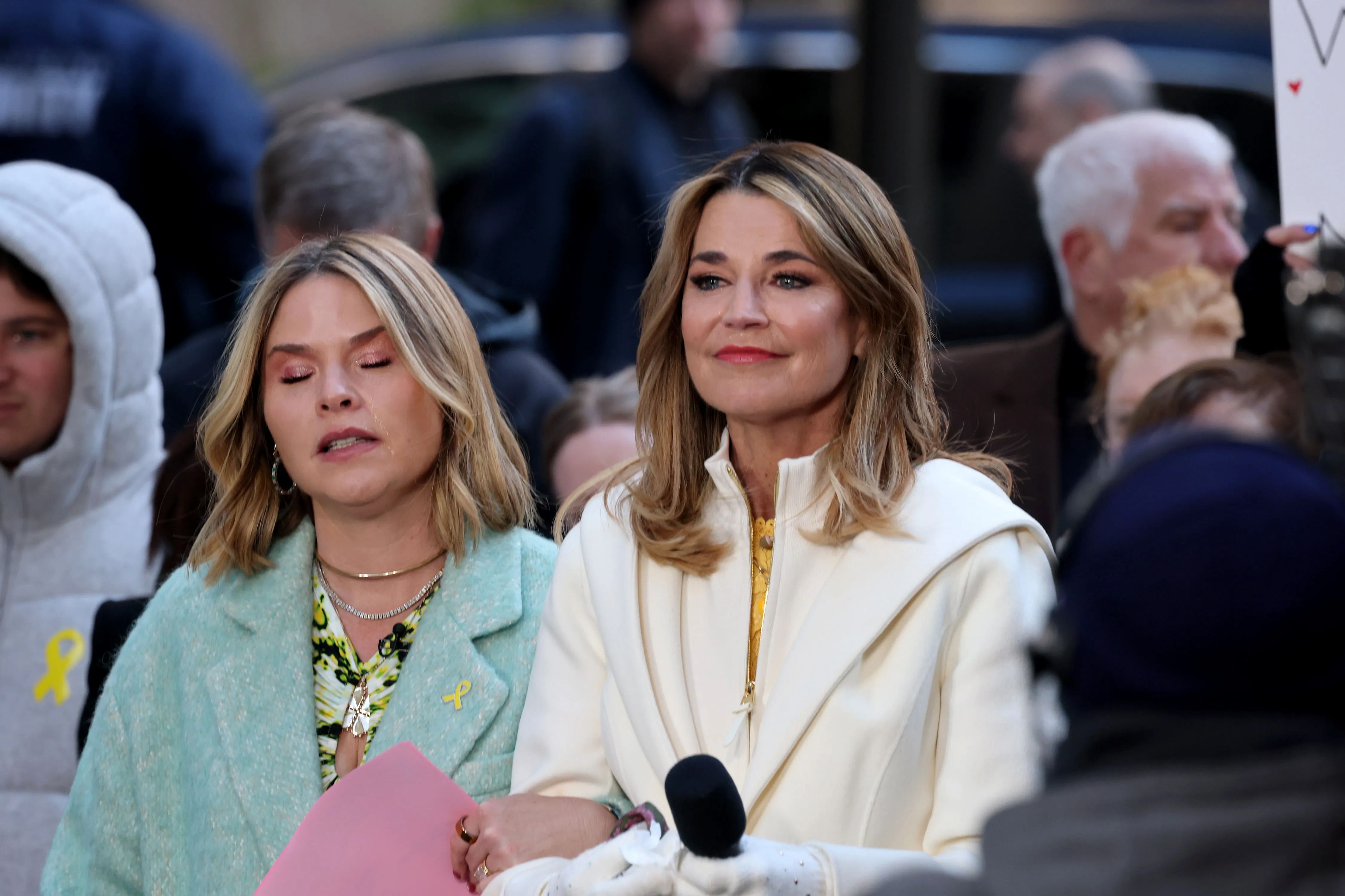 Savannah Guthrie, wearing a white coat, with another woman who is crying, on the "Today" show plaza.