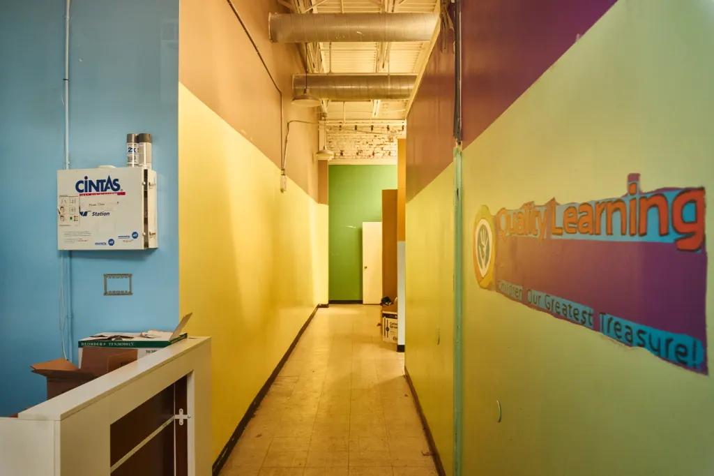 A hallway in the Quality Learning Center daycare with a "Quality Learning Children Our Greatest Treasure!" sign on the right wall.
