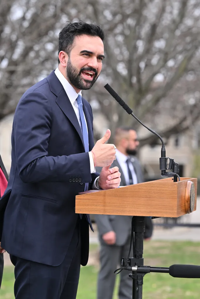 NYC Mayor Zorhan Mamdani speaking at a press conference, gesturing with his hands.