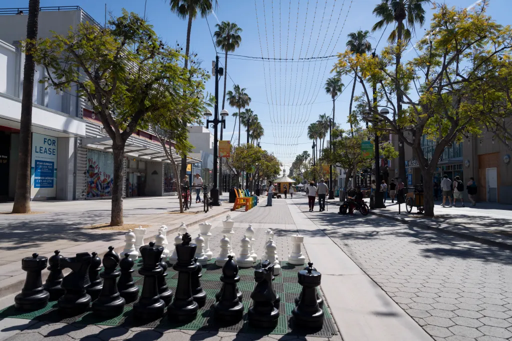 The 3rd Street Promenade in Santa Monica with an outdoor chess set and "For Lease" signs on storefronts.