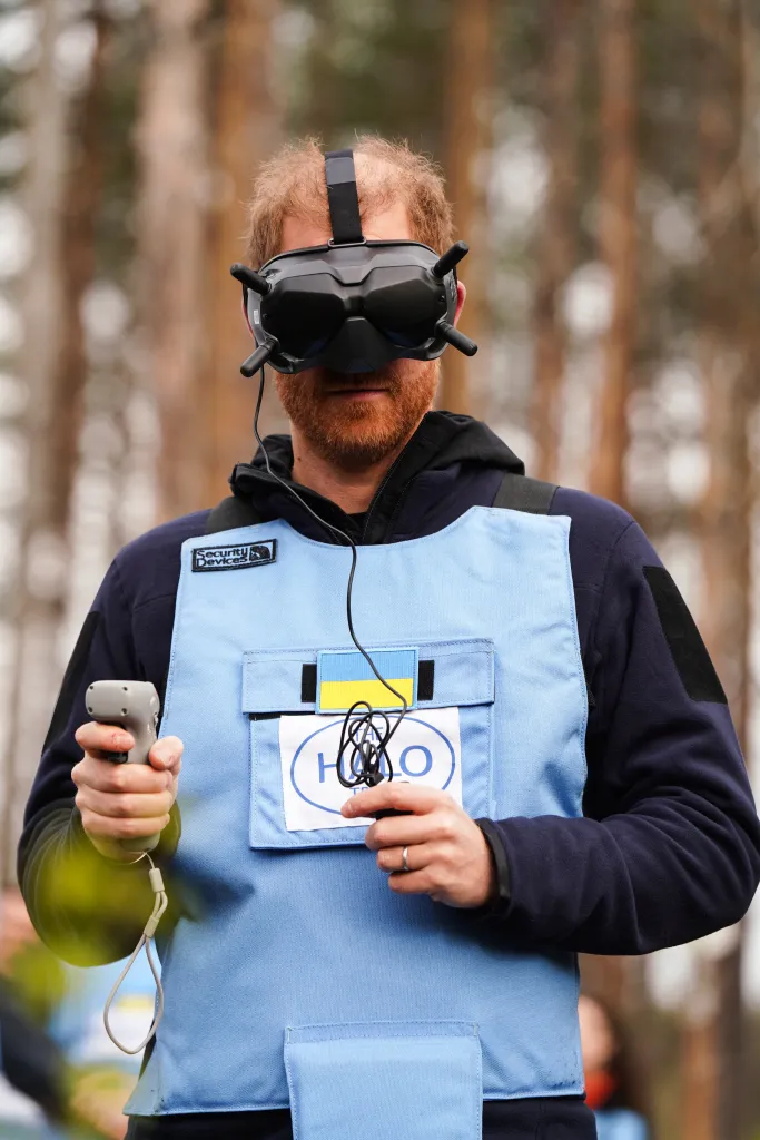 Prince Harry wearing VR goggles and holding a controller, testing demining technology.
