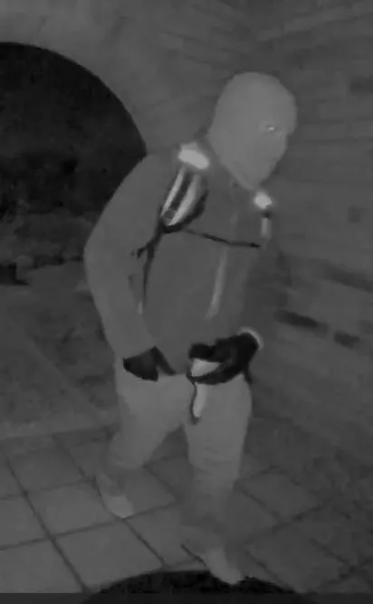 Surveillance image of a suspect wearing a balaclava, jacket, gloves, and pants.