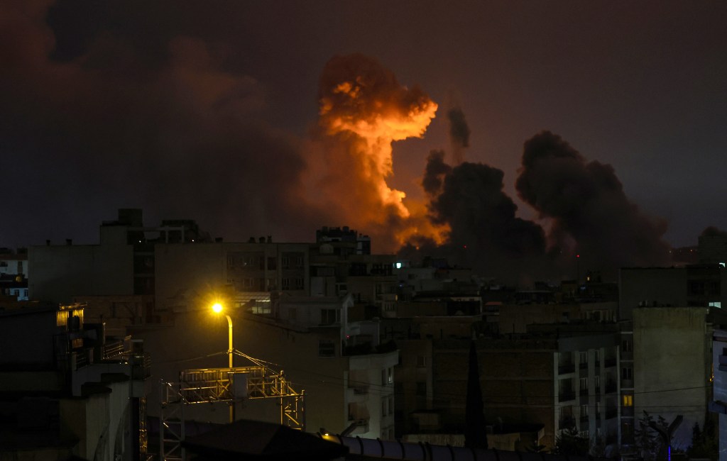A nighttime view of Tehran with a large orange plume of smoke rising above buildings from reported explosions.