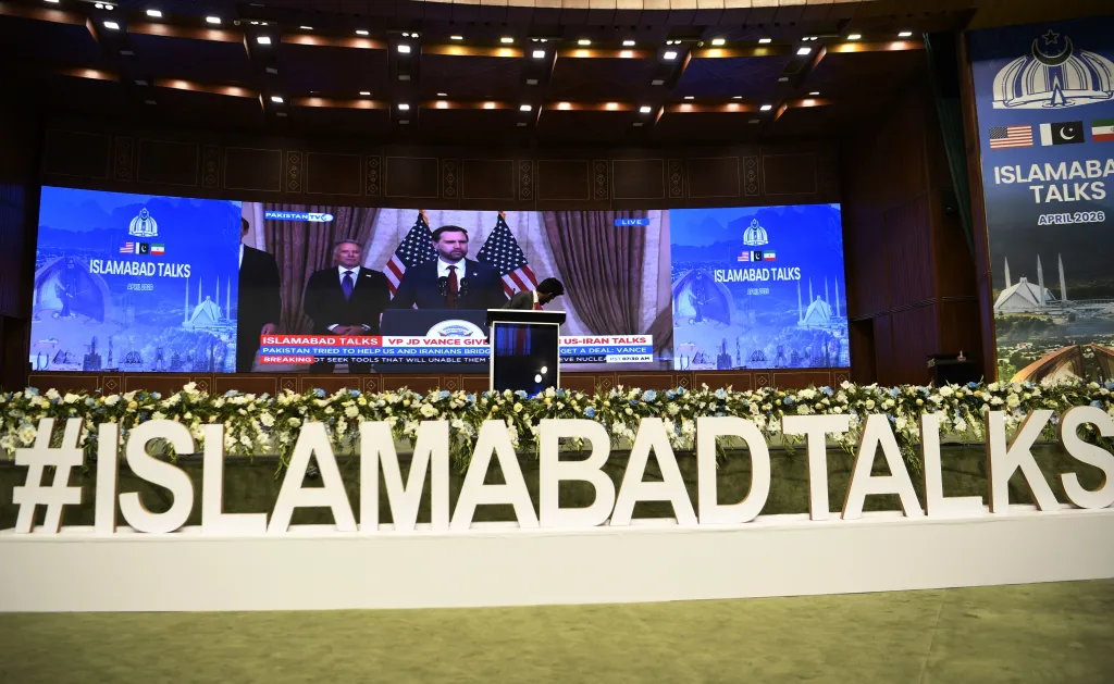 Stage with a large screen showing US Vice President JD Vance speaking, with "ISLAMABAD TALKS" and country flags displayed.