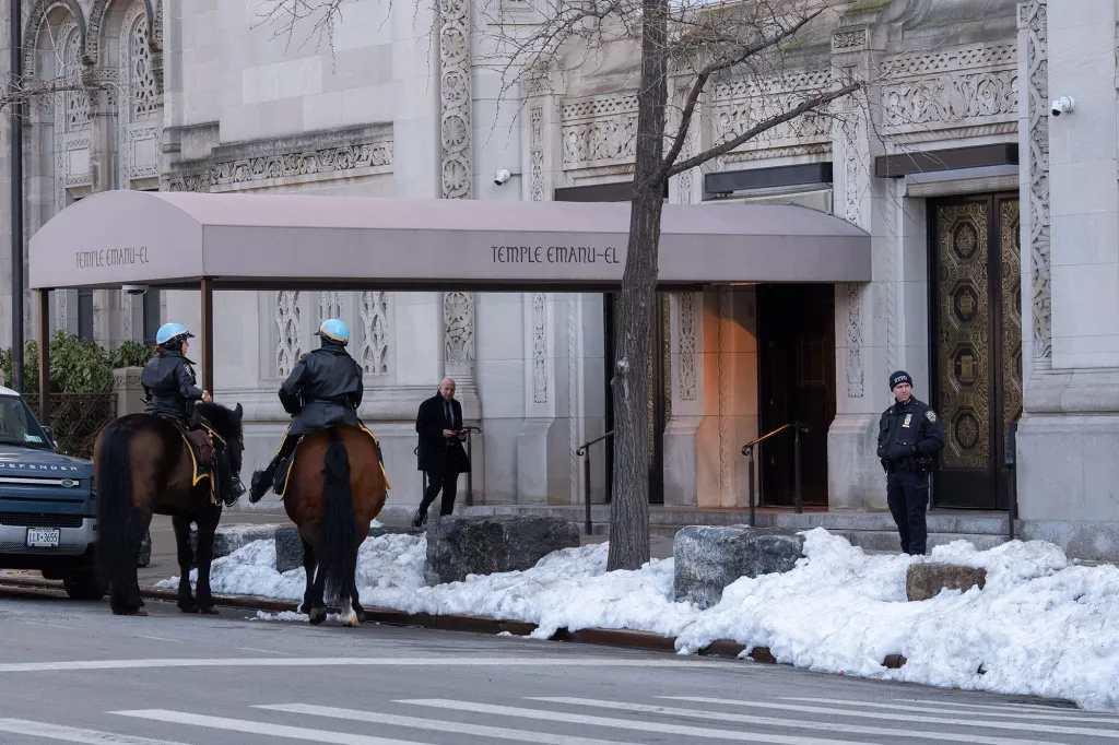 Two NYPD officers on horseback and one officer on foot guard Temple Emanu-El synagogue, with snow on the ground.
