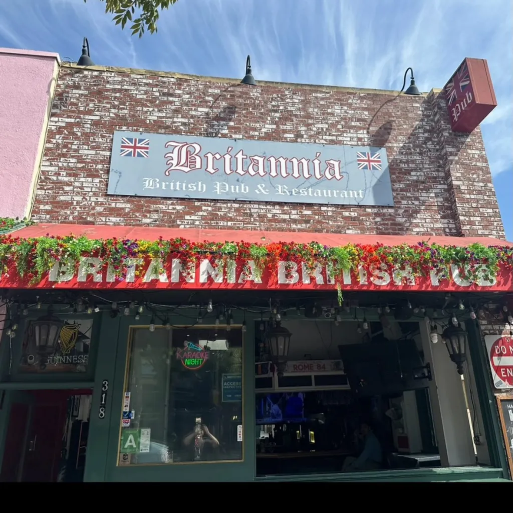 The exterior of Britannia British Pub & Restaurant, a brick building with a red awning adorned with flowers and a sign indicating it's located at 318 Santa Monica Blvd.