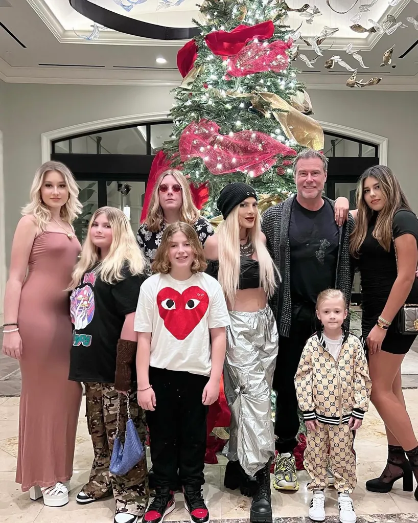 A large family, with a man and a woman surrounded by six children of varying ages, standing in front of a decorated Christmas tree.