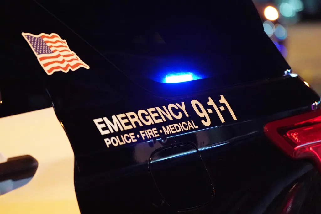 A close-up of a police car with "EMERGENCY 9-1-1 POLICE • FIRE • MEDICAL" written on its side, along with an American flag decal.