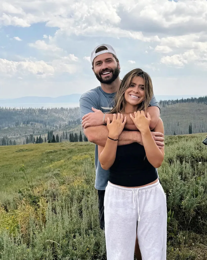 Taylor Frankie Paul and Dakota Mortensen smiling, with him embracing her from behind, set against a mountainous landscape.