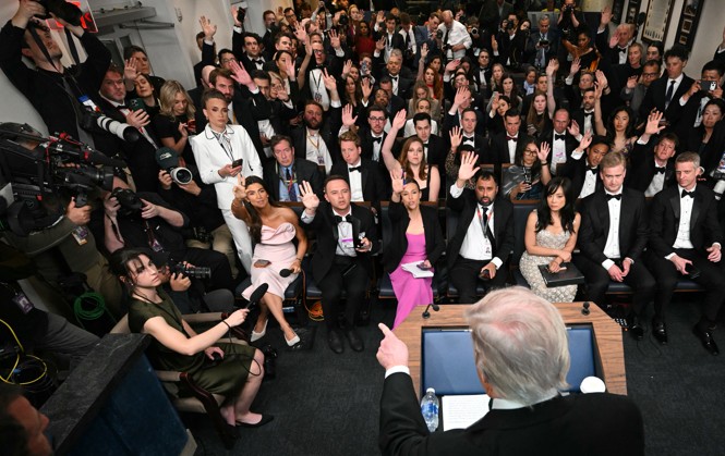 Room full of journalists in evening wear and tuxedos raising hands to ask Trump questions as he points at one of them