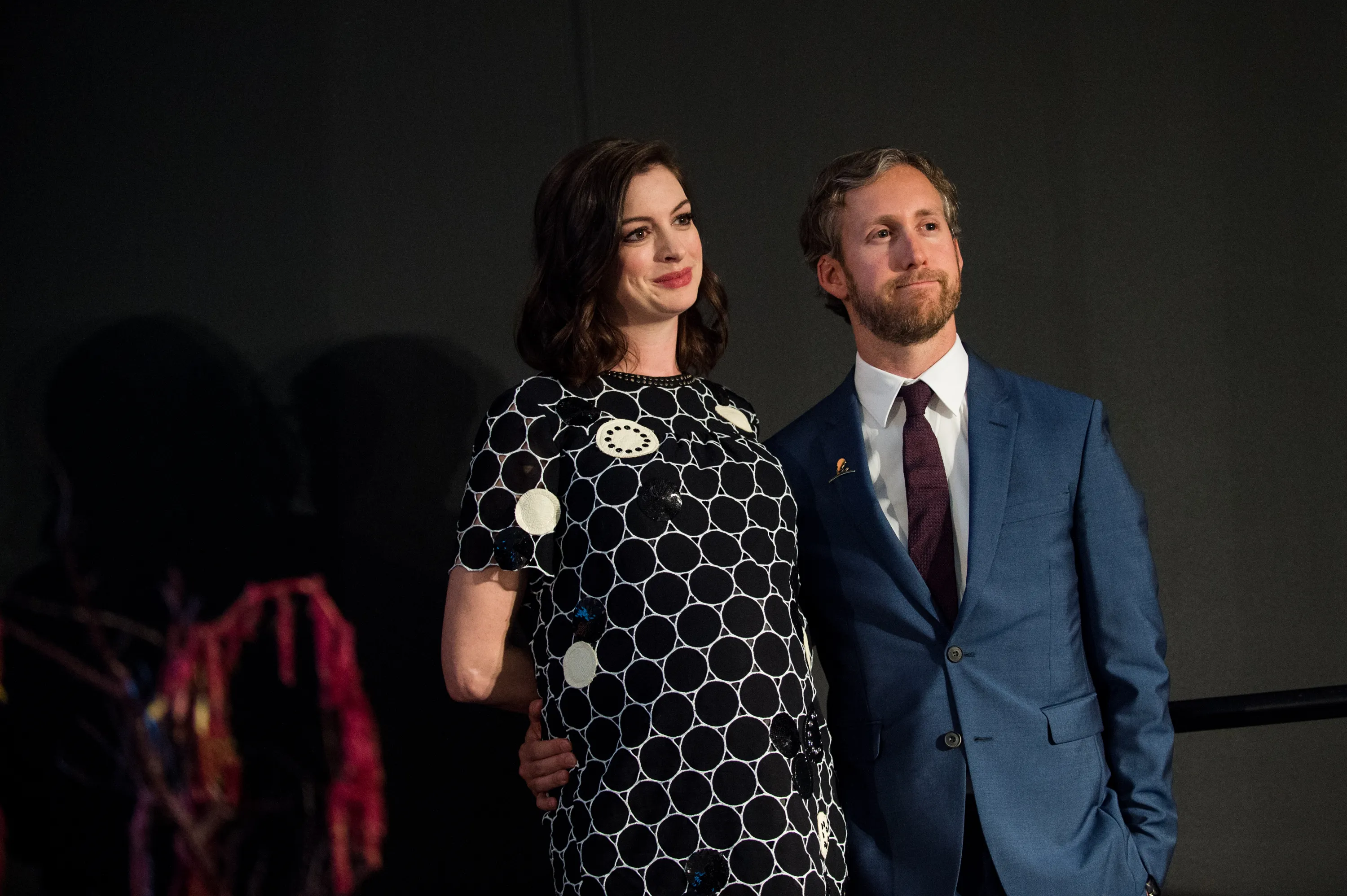 Anne Hathaway and Adam Shulman stand together, looking to the right.