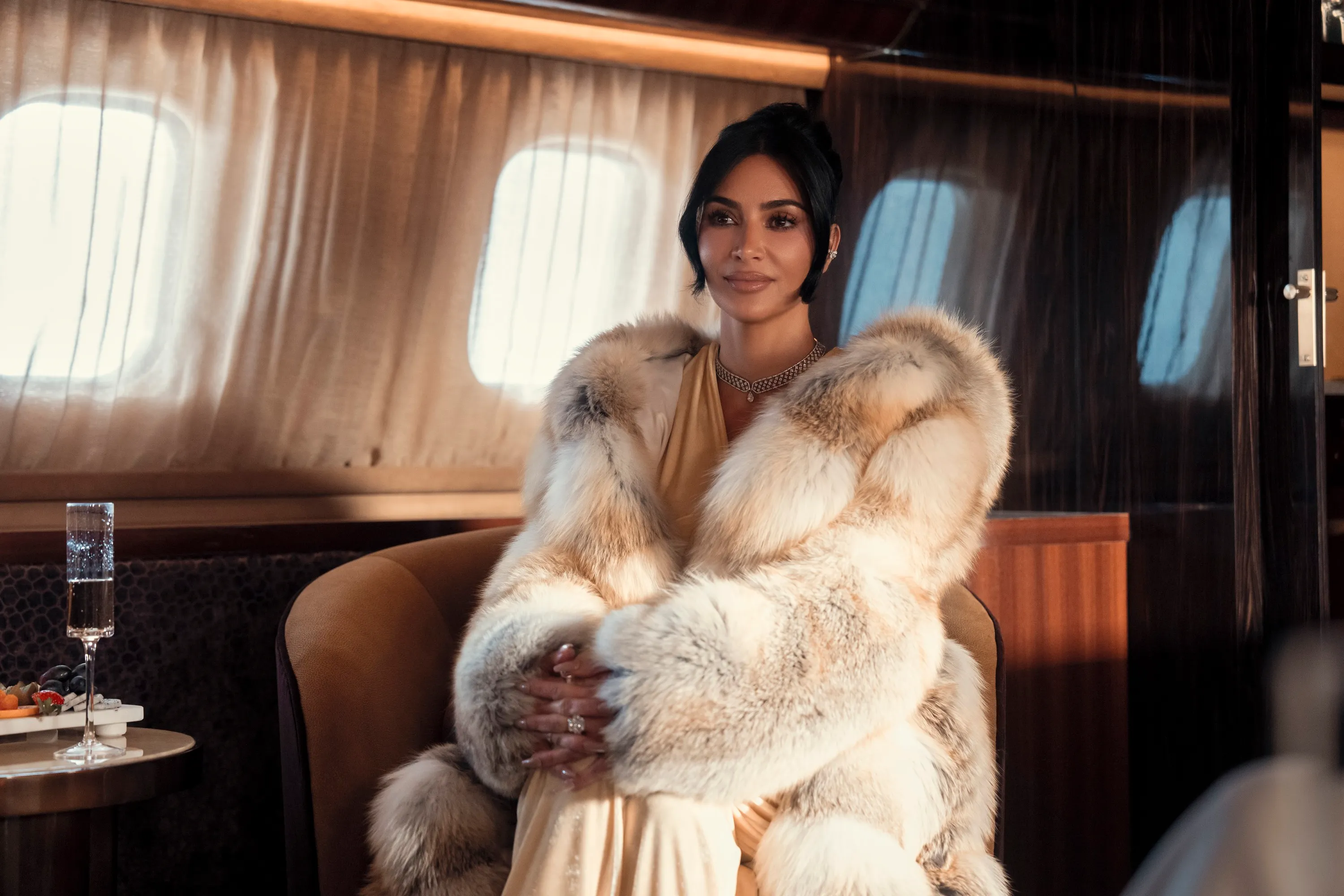 Kim Kardashian in a fur coat sitting on a plane.