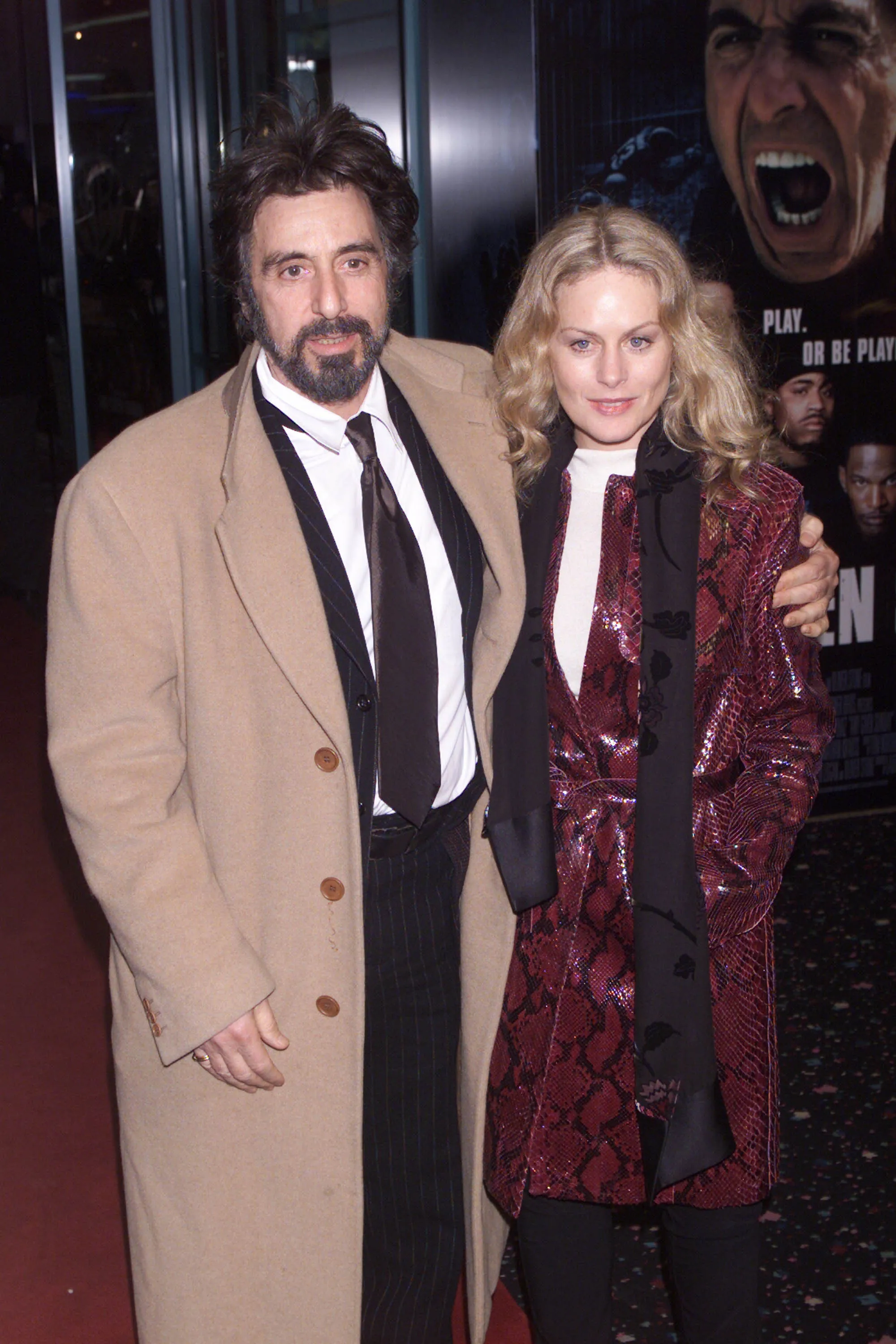 Al Pacino in a camel coat with his arm around Beverley D'Angelo in a red snakeskin jacket.