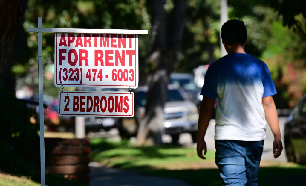 "Apartment For Rent" sign with phone number and "2 BEDROOMS" on a street.