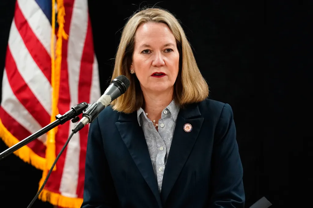 Arizona Attorney General Kris Mayes speaking at a podium with an American flag in the background.