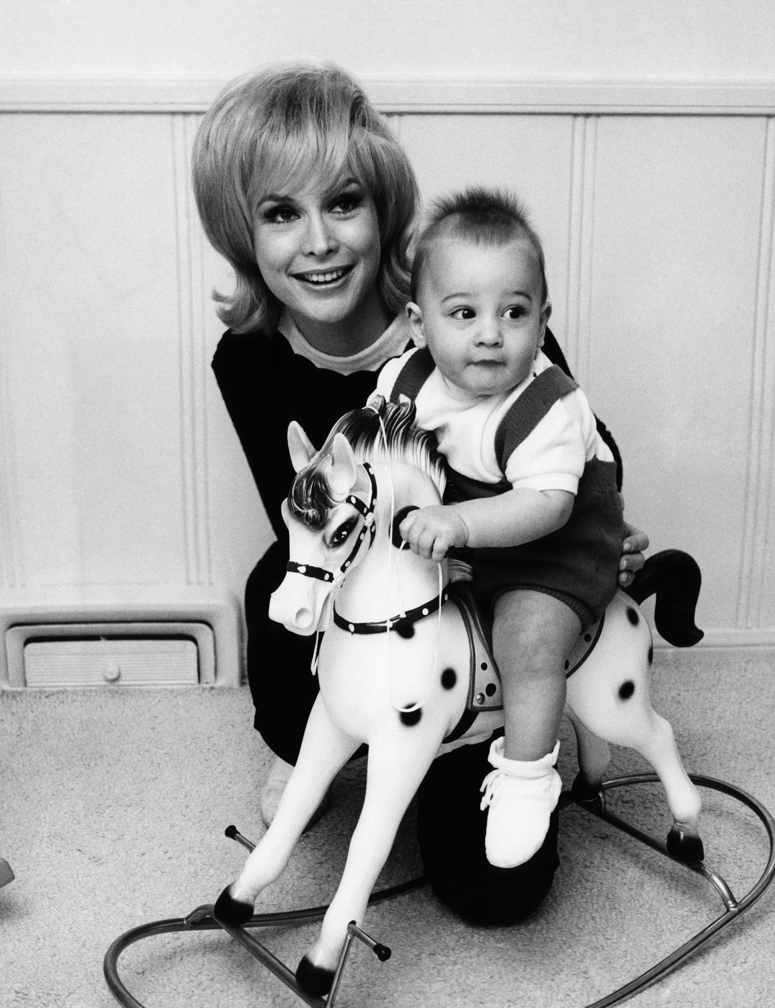 Barbara Eden smiling with her son Matthew Ansara on a rocking horse.