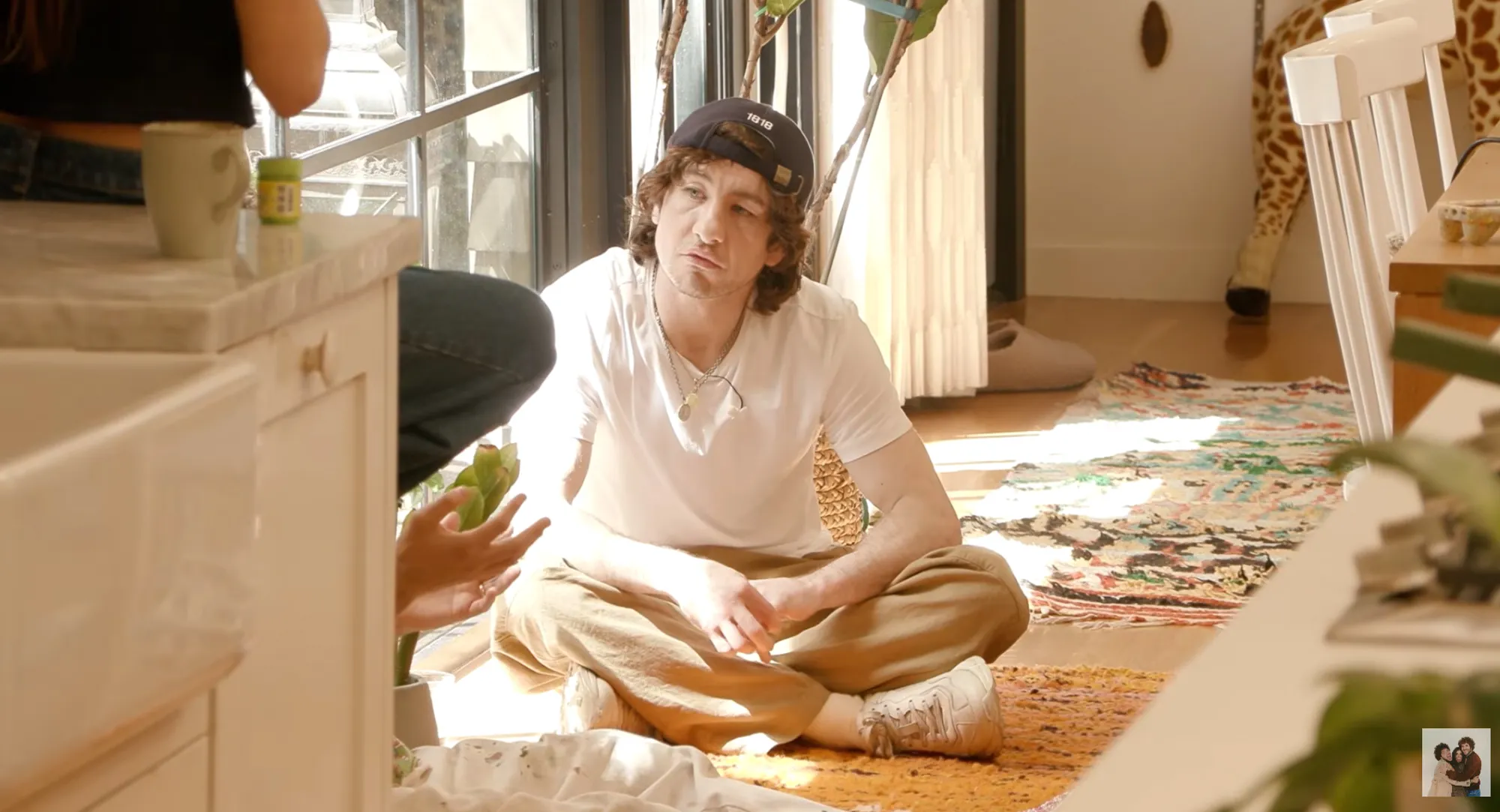 Barry Keoghan sits cross-legged on a patterned rug, looking towards someone out of frame.