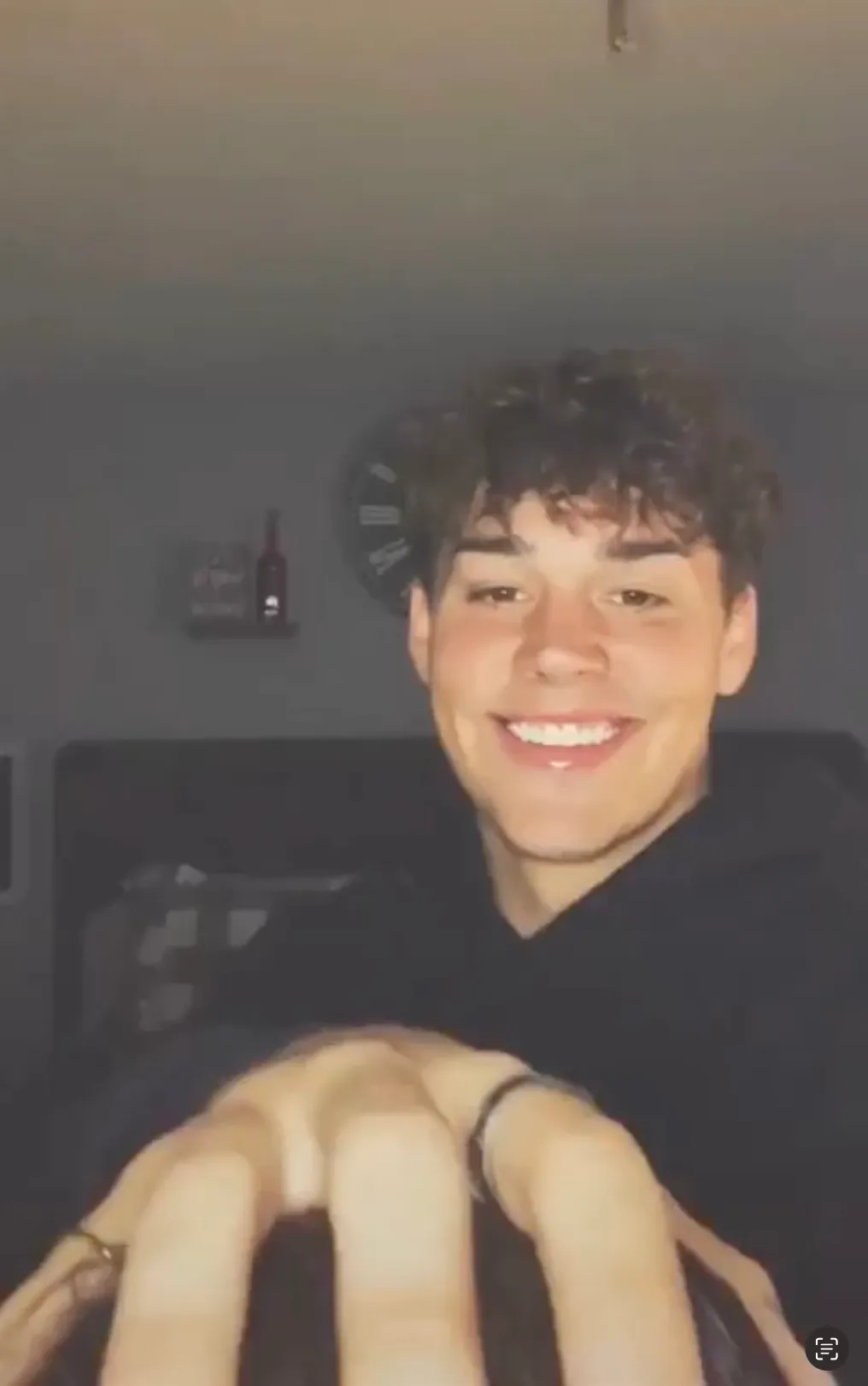 Noah Beck smiling at the camera while a hand reaches up from out of frame.