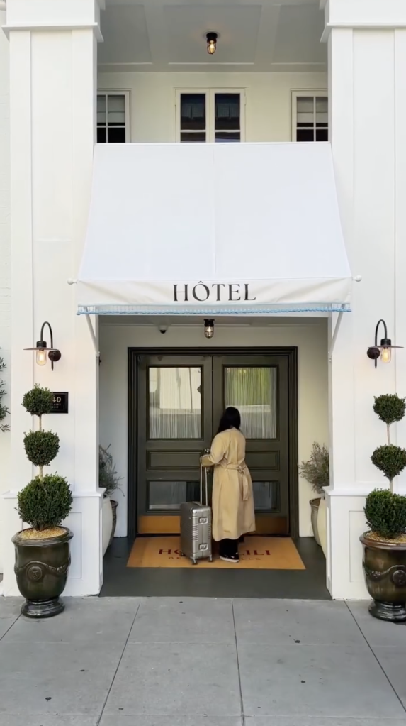 A person with a suitcase approaches the entrance of a building with an awning that says "HÔTEL".