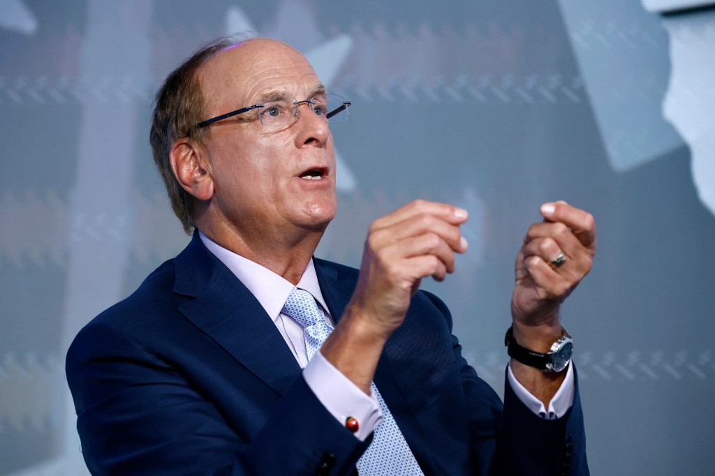 BlackRock CEO Larry Fink in a dark blue suit and light blue patterned tie, wearing glasses, speaking with his hands gesturing.