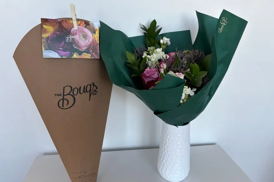 A bouquet of flowers from The Bouqs in a vase next to a brown bag.