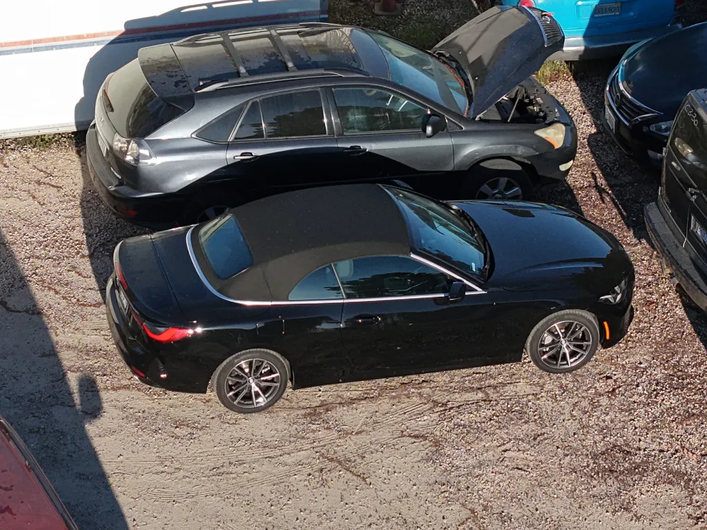Black convertible car and grey SUV in a tow yard.