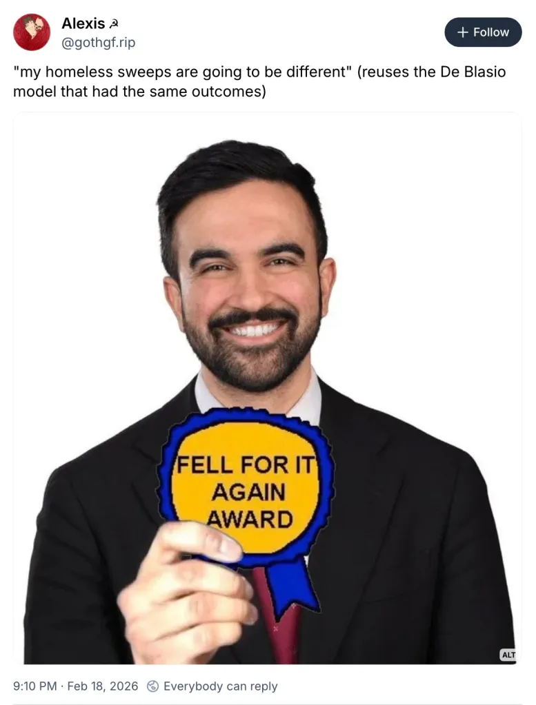 Zohran Mamdani in a suit holding a blue and yellow "Fell for it again award" badge.