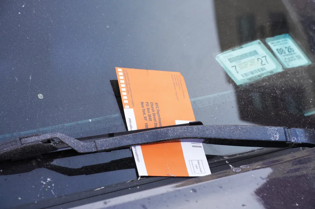 A parking ticket from the NYC Department of Finance tucked under a car's windshield wiper.