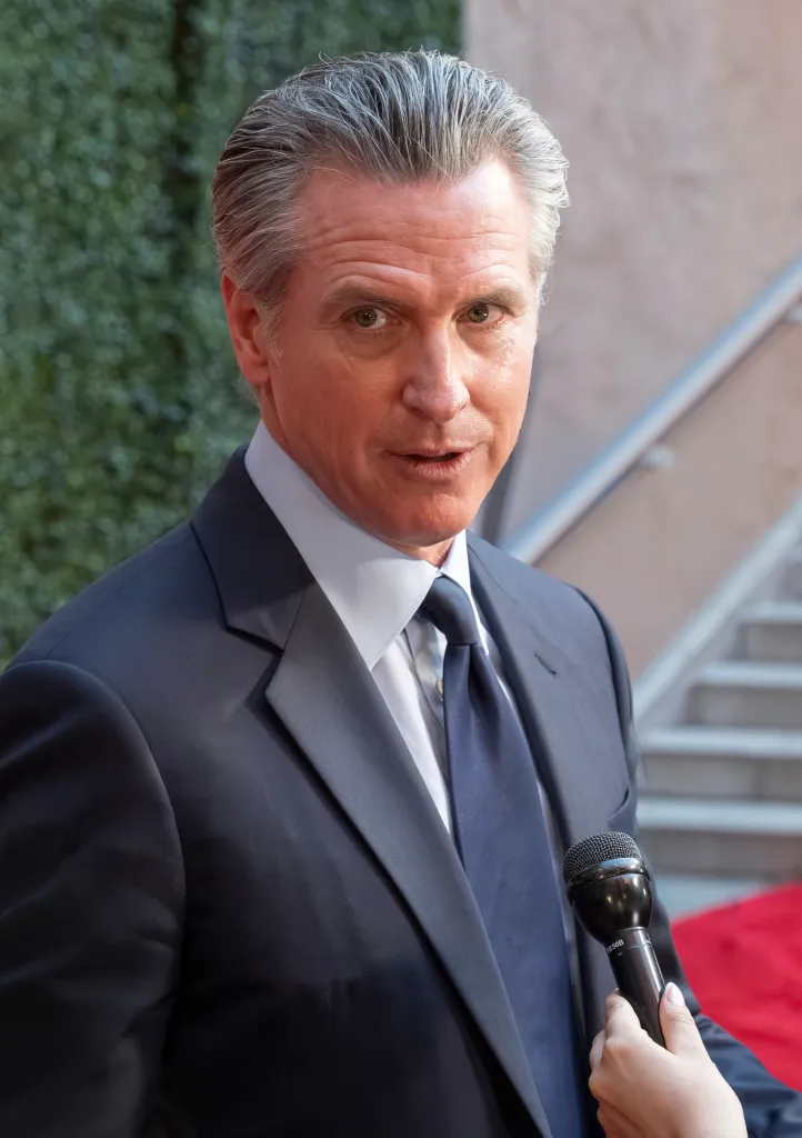 California Governor Gavin Newsom speaking into a microphone at the 19th Annual California Hall of Fame Ceremony.