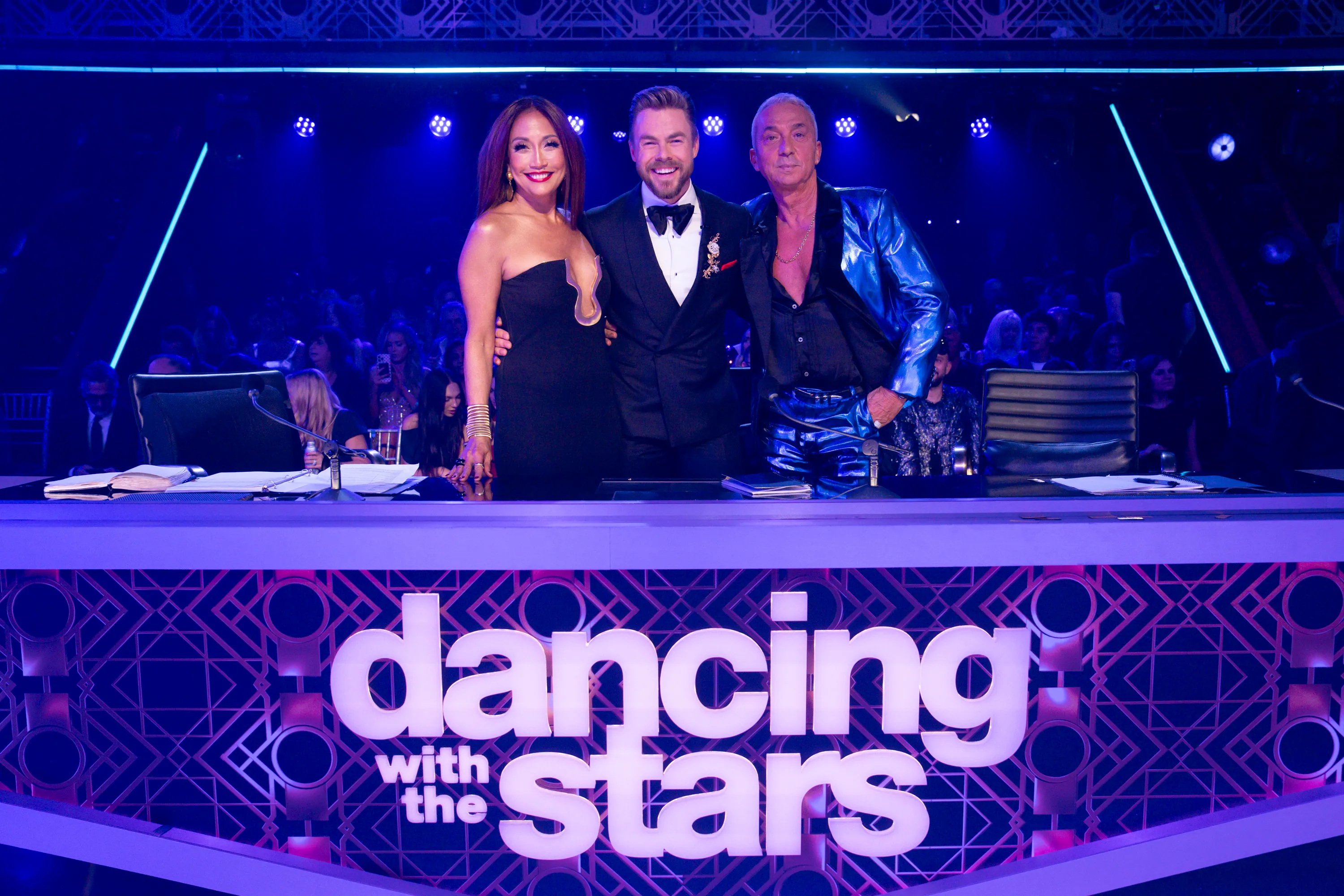 Carrie Ann Inaba, Derek Hough, and Bruno Tonioli stand behind a 