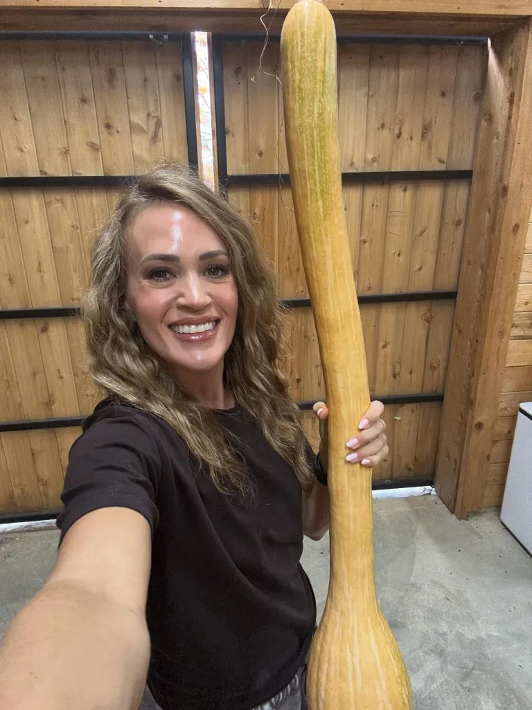 Carrie Underwood holding a very large, long squash.
