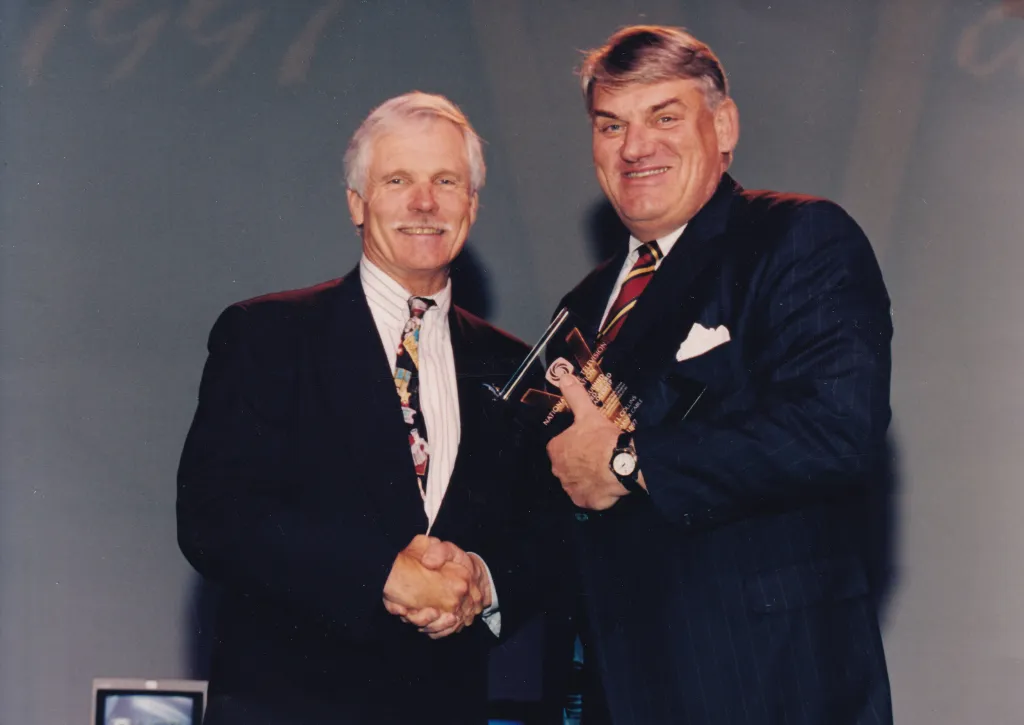 Ted Turner (left) shaking hands with Joseph J. Collins (right) as Collins receives the Distinguished Vanguard Award.