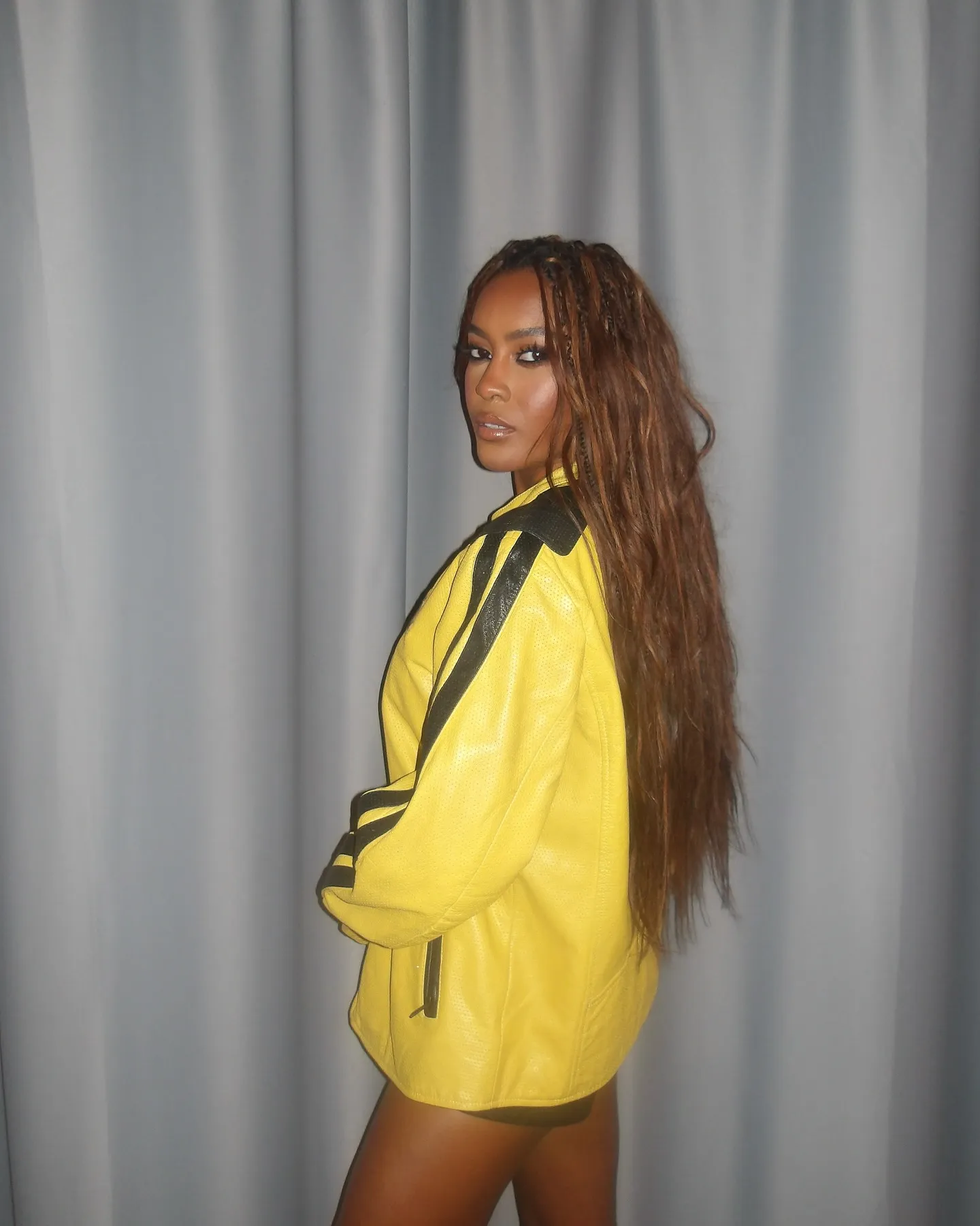 Ciara Miller wearing a yellow leather jacket with black stripes.