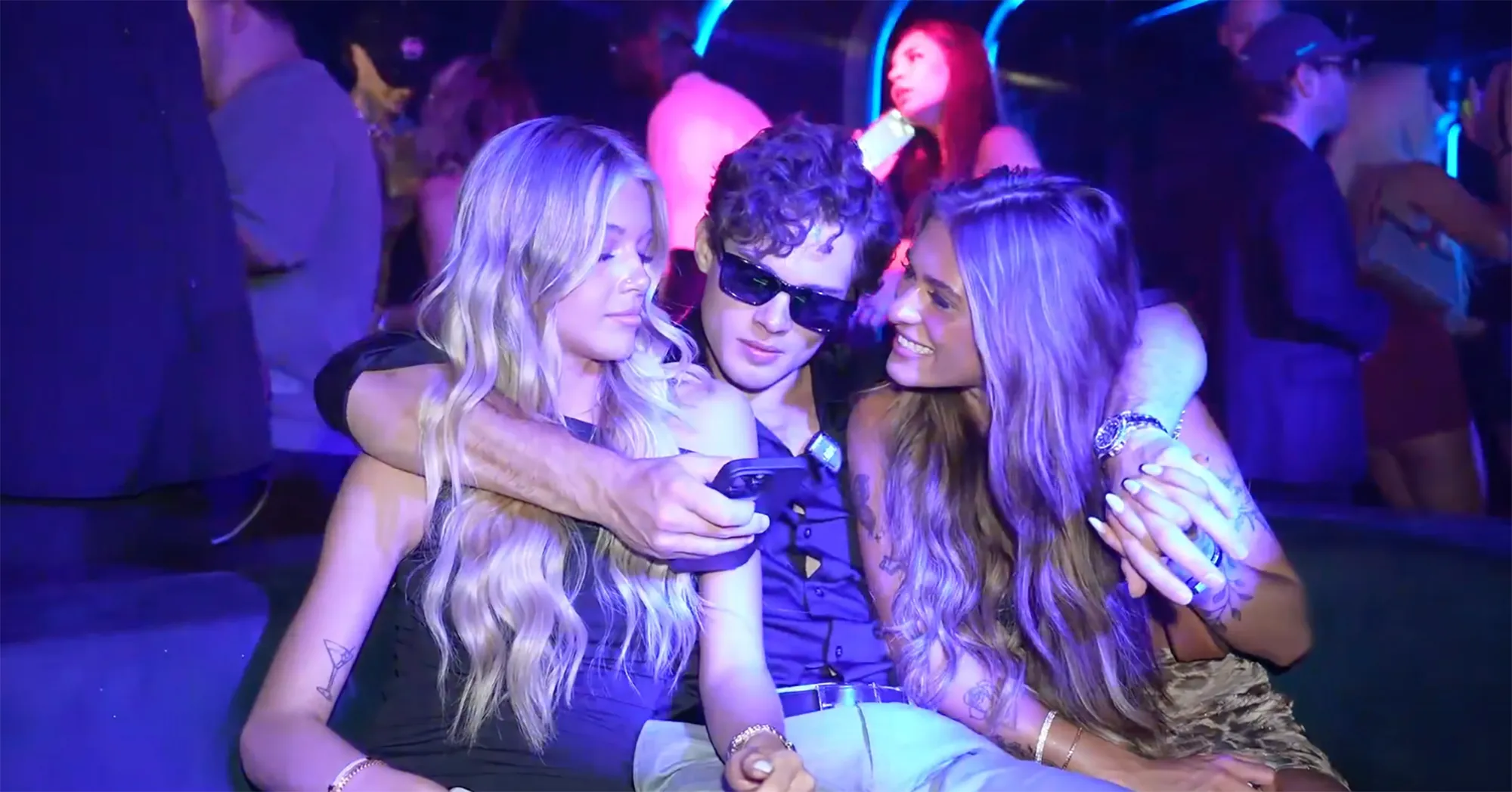 Clavicular in sunglasses holding two women in a Miami club.