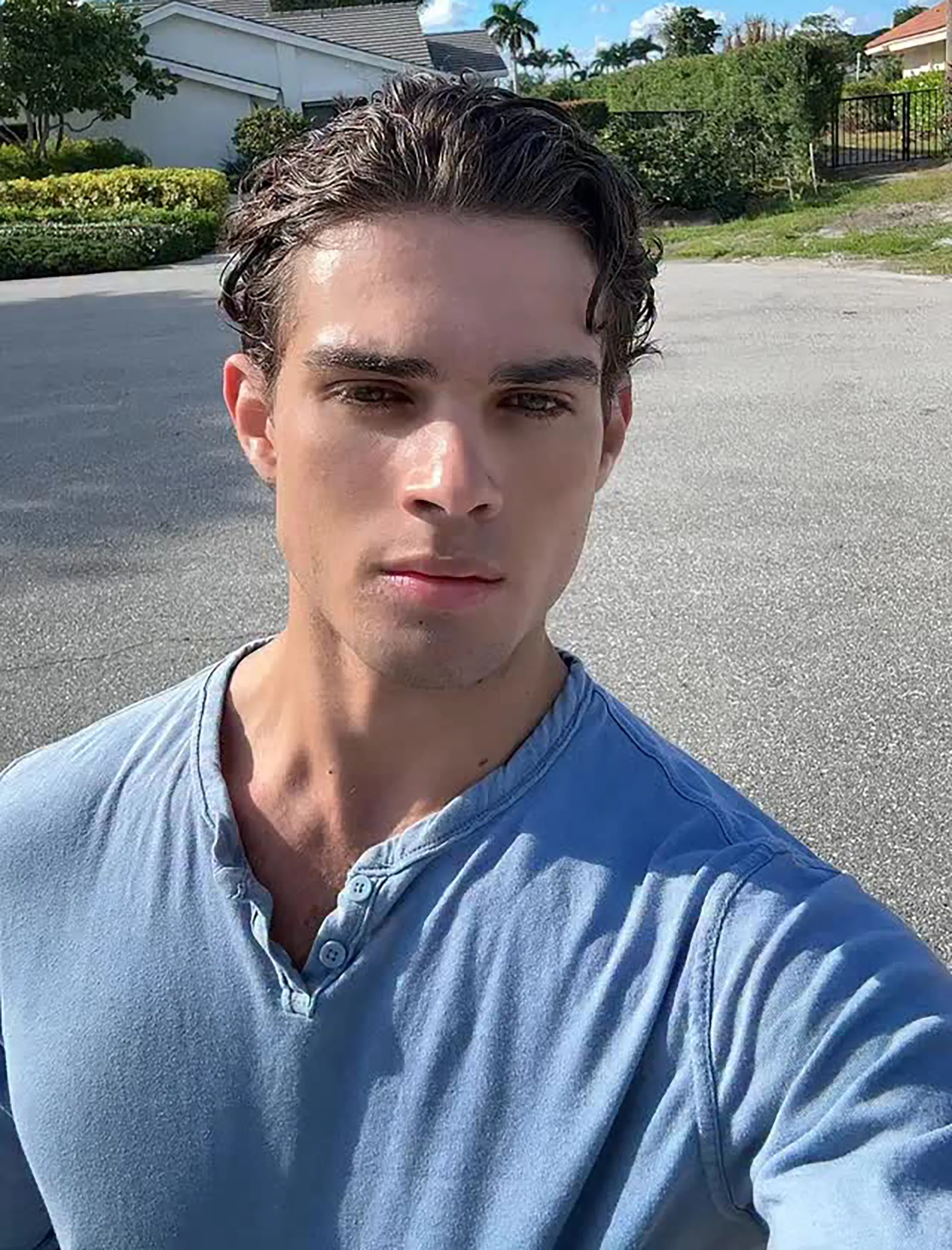 A man with short brown hair and a blue shirt posing for a selfie outside.