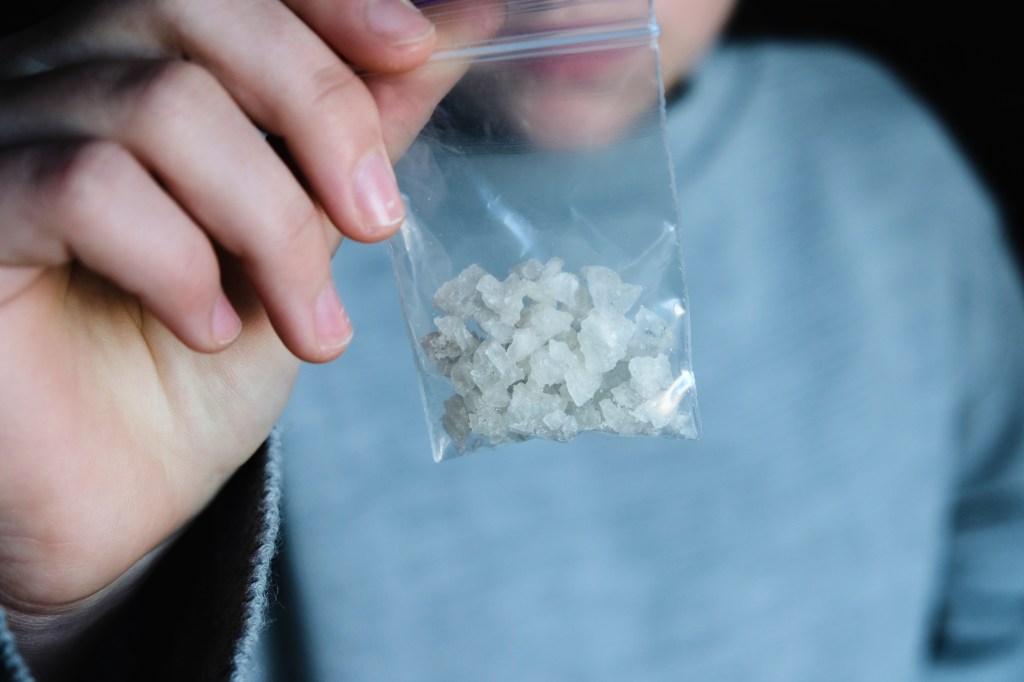 A hand holding a clear plastic baggie filled with white crystals.
