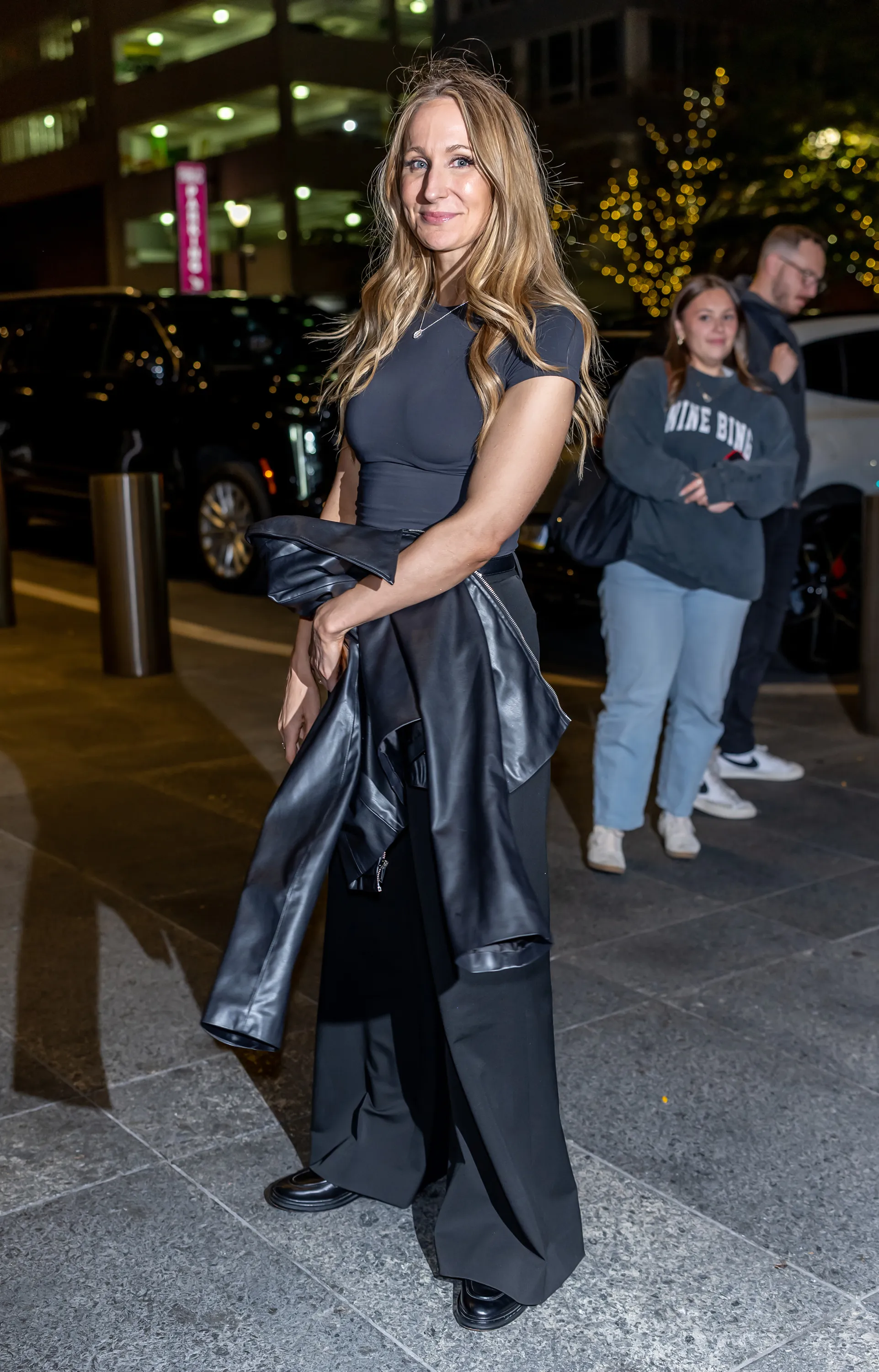 Nikki Glaser in a black shirt, pants, and holding a black leather jacket during her "Alive and Unwell Tour".