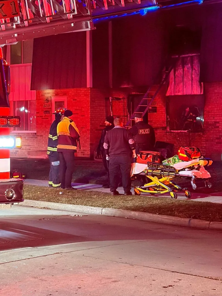 Emergency responders and a stretcher are outside a burning Wisconsin apartment building.