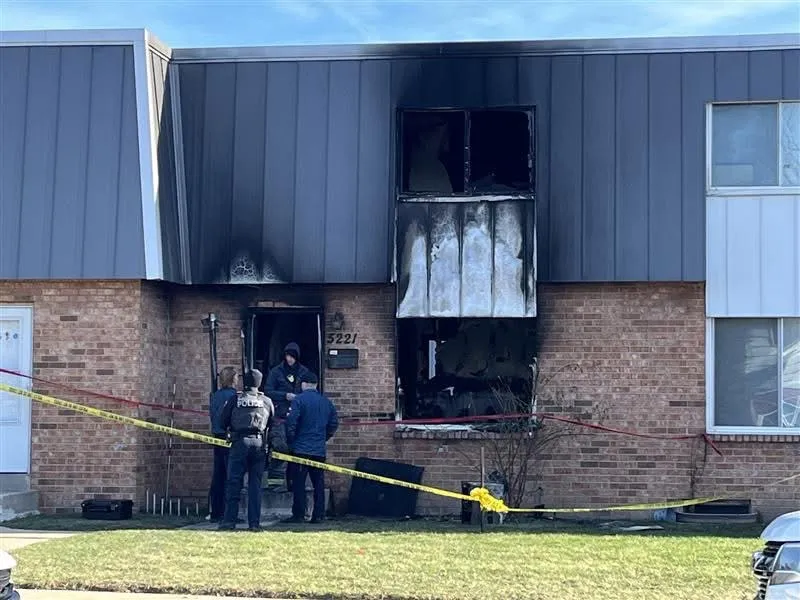 A two-story apartment building with fire damage around a window and front door on the right, with police and caution tape present.