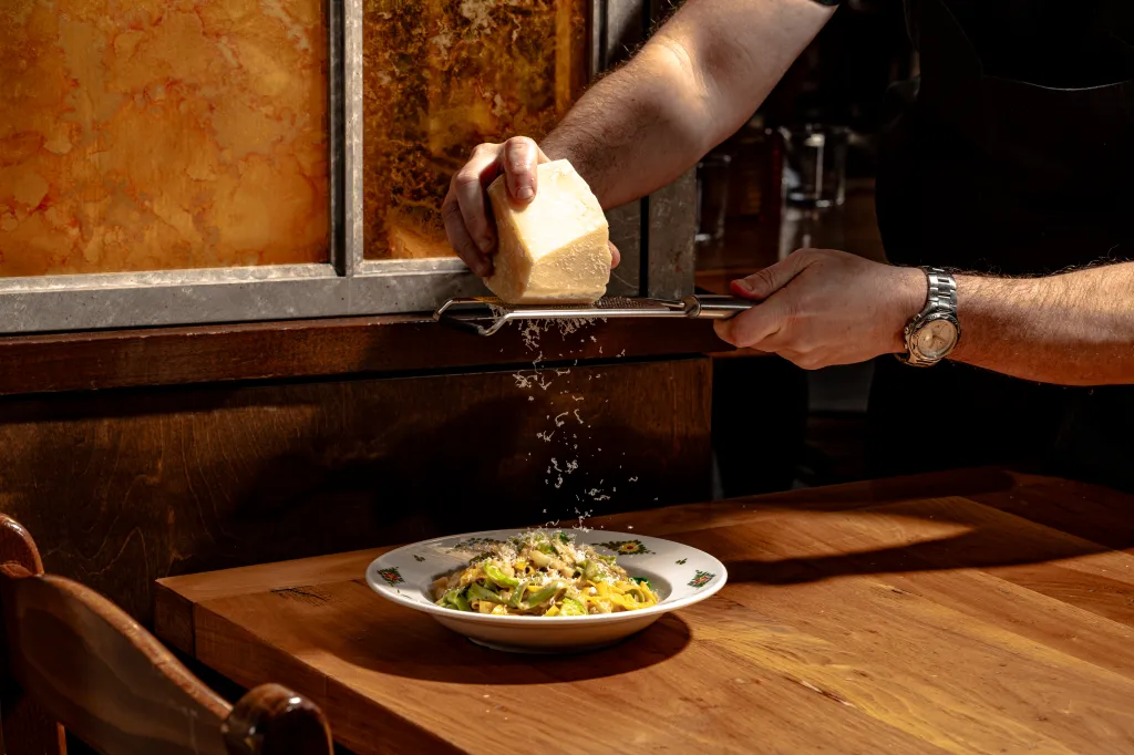 A person's hands grating parmesan cheese over a plate of pasta.