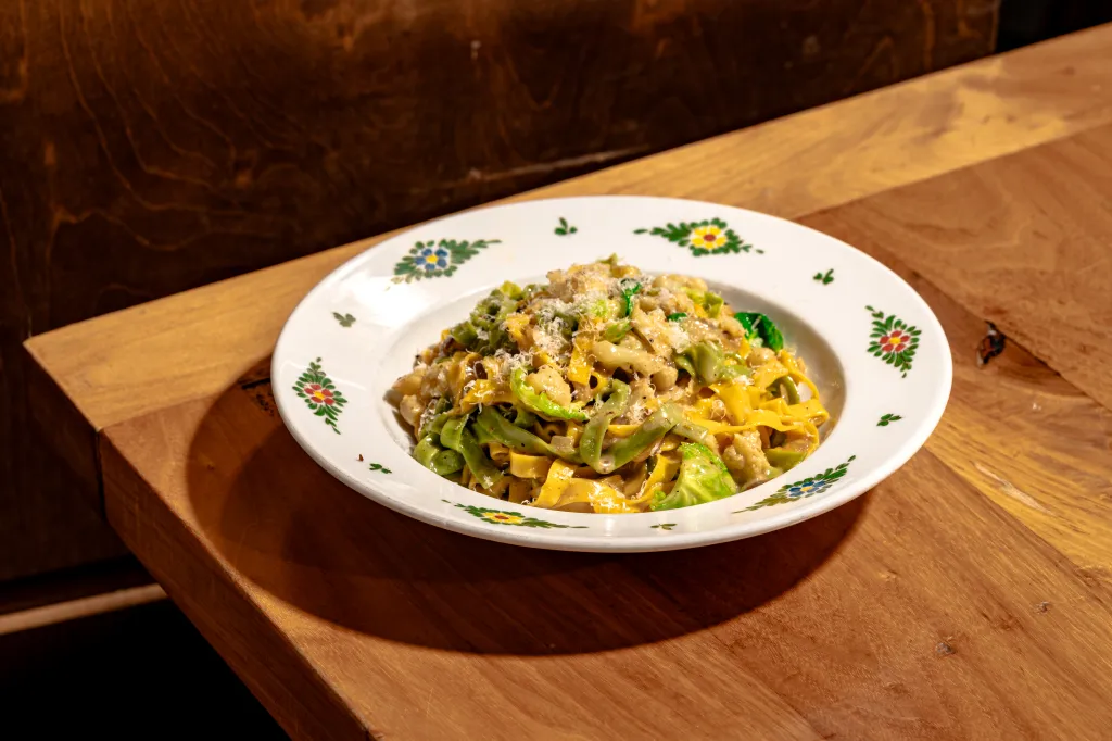 A plate of green and yellow pasta with vegetables and shredded cheese on a wooden table.